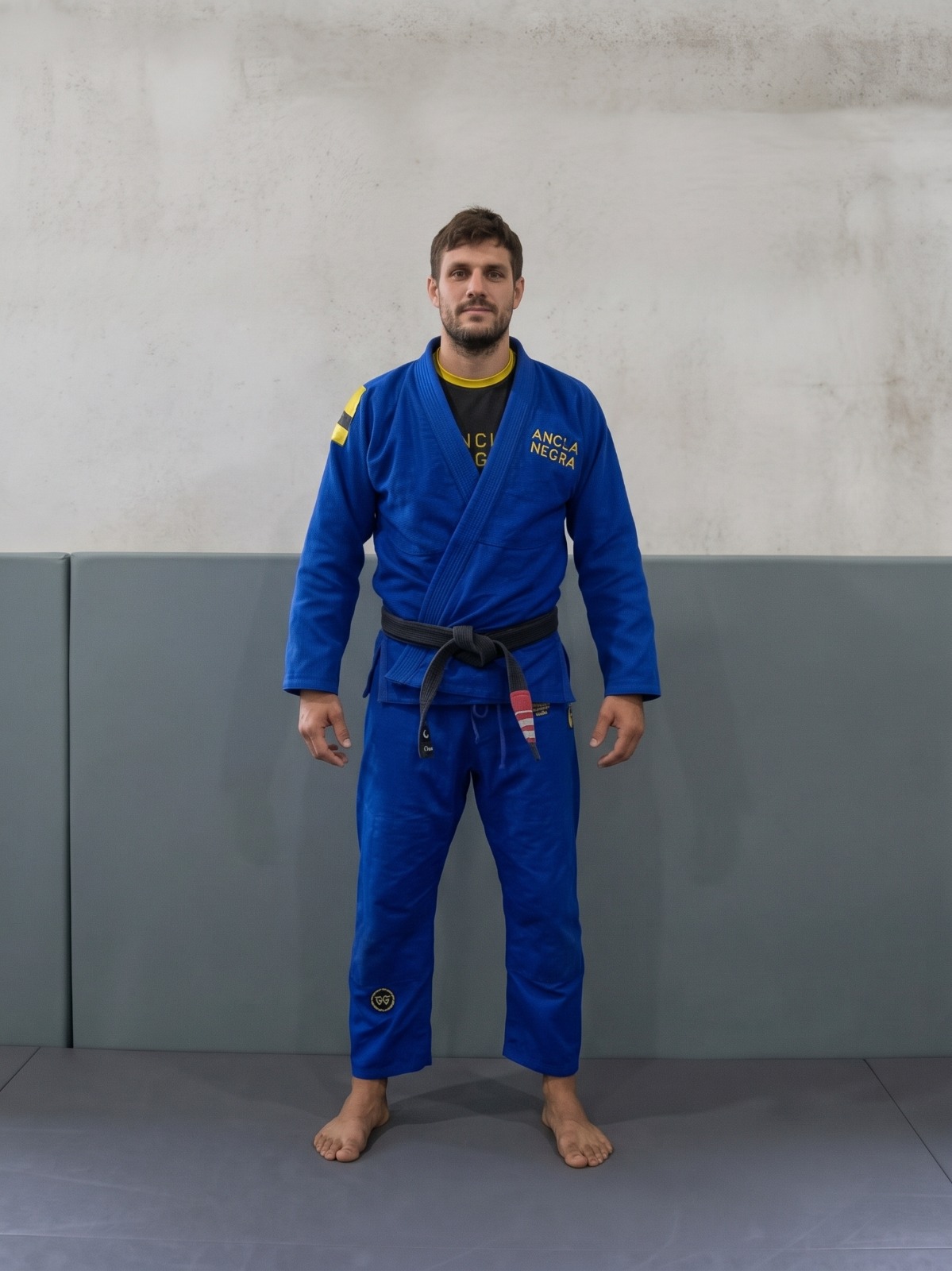 Franco Marini de pie, con kimono azul Ancla Negra y cinturón negro, frente a una pared de hormigón