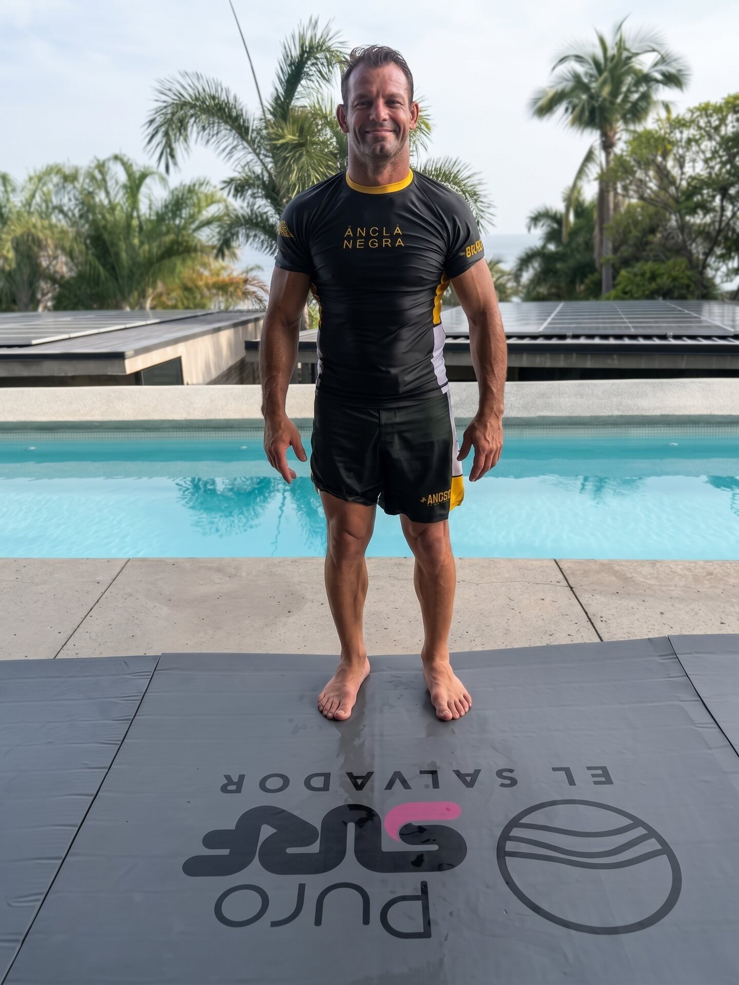 Martín Passeri de pie junto a una pileta, con remera Ancla Negra y palmeras de fondo